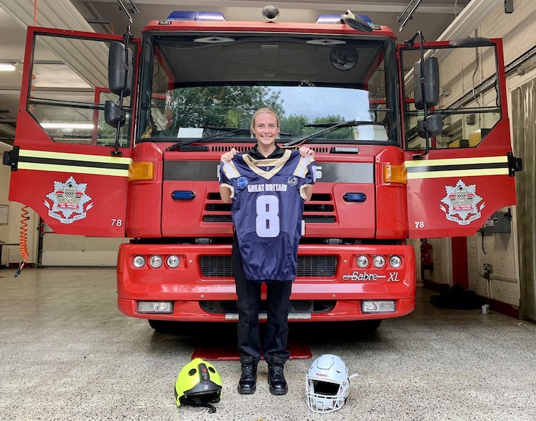 Harley stands in front of a fire engine, holding her American football shirt with her fire and football helmets at her feet. (WMFS)